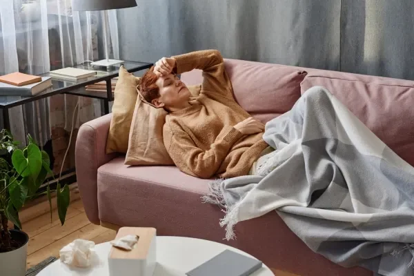 Woman suffering migraine on the couch with tissues