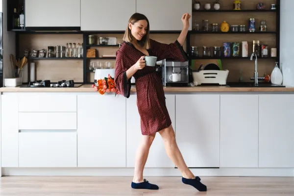 Energetic woman enjoying her morning coffee while smiling and dancing